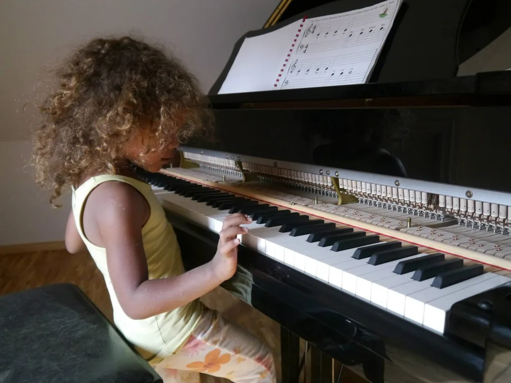 Mädchen mit Locken spielt am Flügel, auf dem Notenpult ein Anfängerheft
